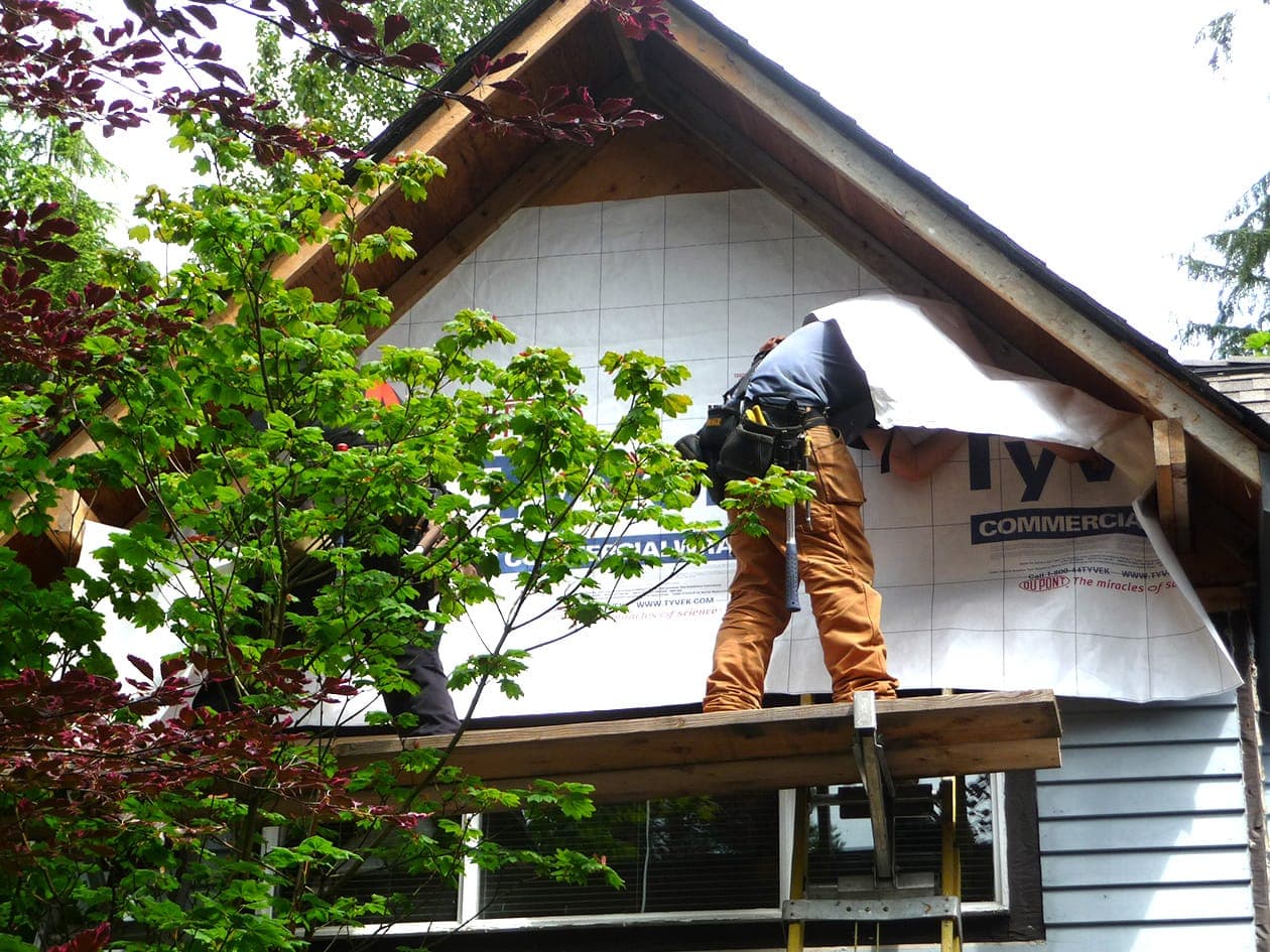 Workers wrapping a gable in building wrap before the new siding